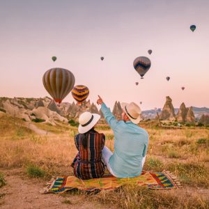 Cappadocia Turkey during sunrise, couple mid age men and woman on vacation in the hills of Goreme Capadocia Turkey, men and woman looking sunrsise with hot air balloons in Cappadocia Turkey